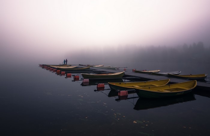 Boats docked on a misty lake with two people on the dock