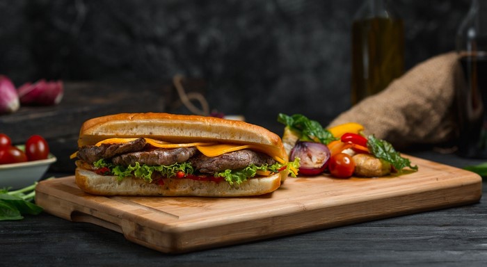 Steak sandwich with cheese and vegetables on a cutting board