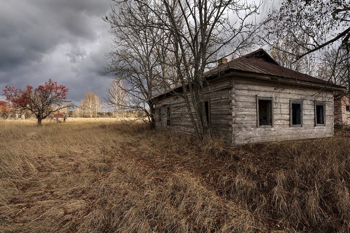 Abandoned wooden house in a dry field under a cloudy sky