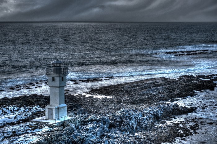 Lighthouse on a rocky shore with stormy sea
