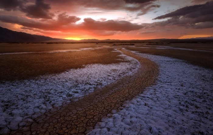 Desert landscape at sunset with cracked earth and mountains