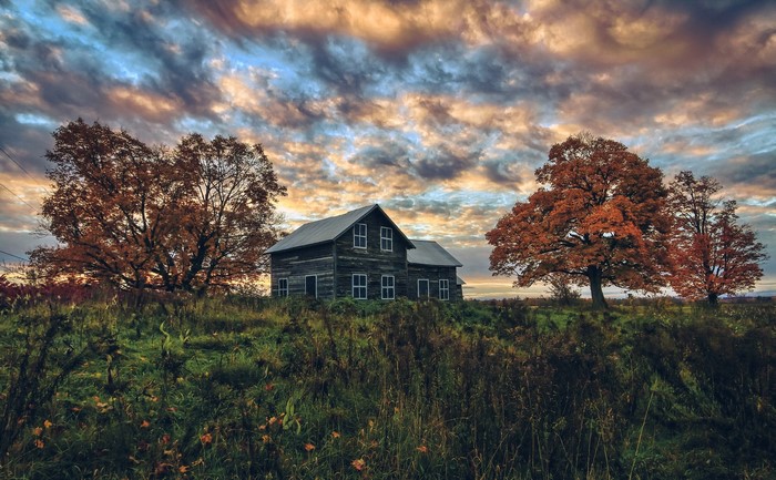 Old wooden house on a hill with autumn trees and dramatic sky