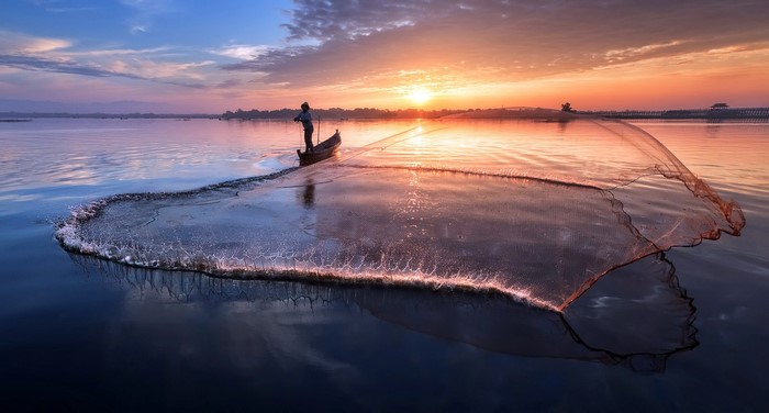 Fisherman casting net at sunset on water