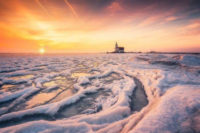 Frozen sea with lighthouse at sunset