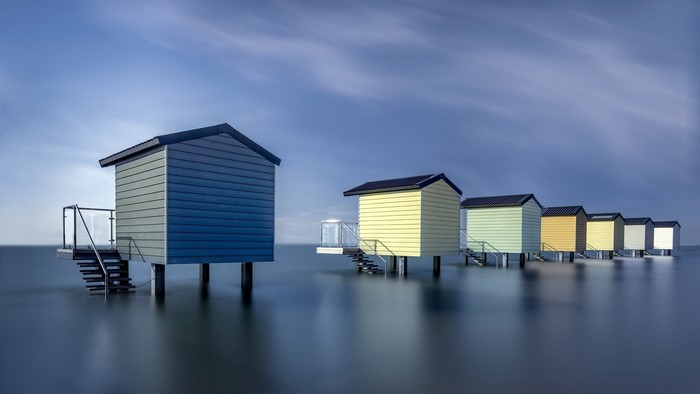 Row of colorful beach huts on stilts in the water
