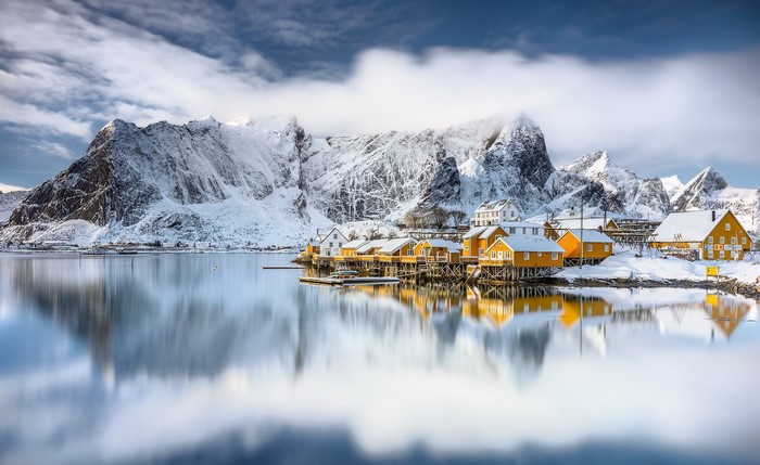 Snowy mountains and yellow houses reflected in water