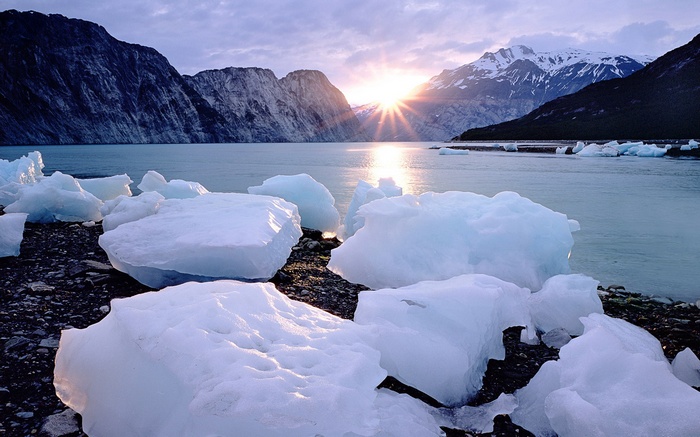 Icebergs on a rocky shore with mountains and sunrise