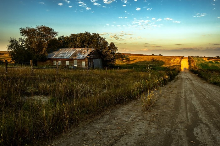 Abandoned house on a dirt road at sunset