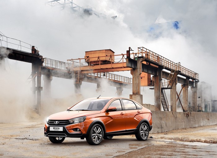 Orange Lada Vesta Cross car in industrial setting with smoke