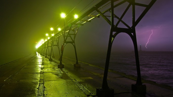 Pier with lights during a lightning storm at night