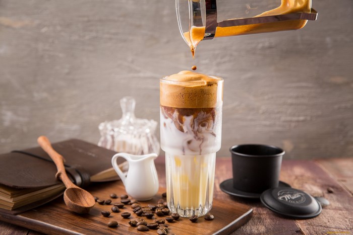 Dalgona coffee being poured into a glass with milk