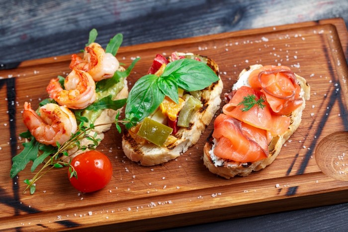 Shrimp, salmon, and vegetable bruschetta on a wooden board