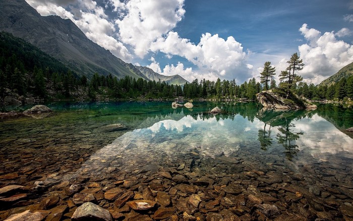 Clear lake reflecting mountains and forest with rocky shore