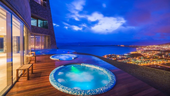 Hot tubs on wooden deck overlooking city lights at dusk
