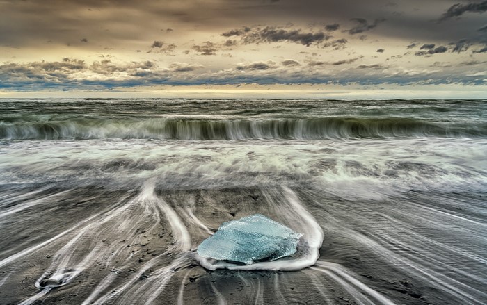 Ice chunk on a beach with waves and cloudy sky