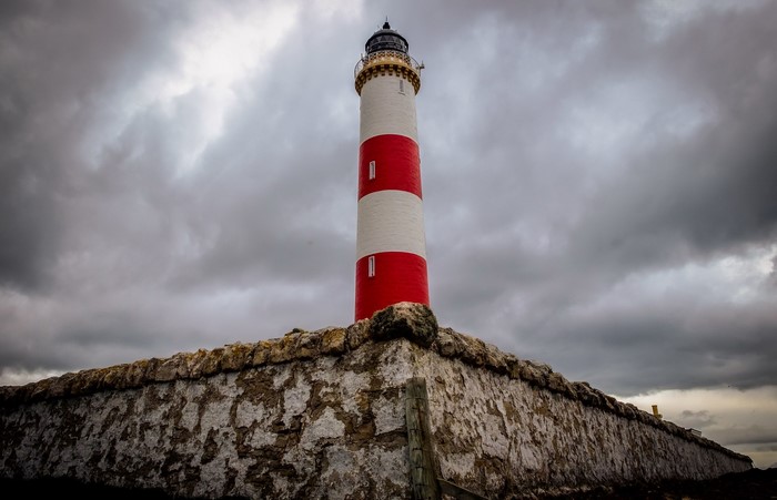 Red and white lighthouse on a stone wall under overcast sky