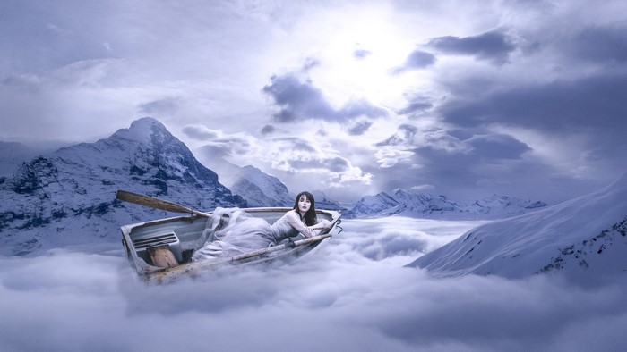 Woman in a boat floating on clouds in mountains