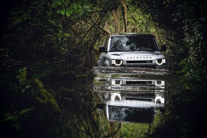 Silver Land Rover Defender driving through water in a forest