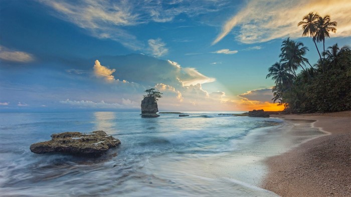 Tropical beach with rock formation and palm trees at sunset