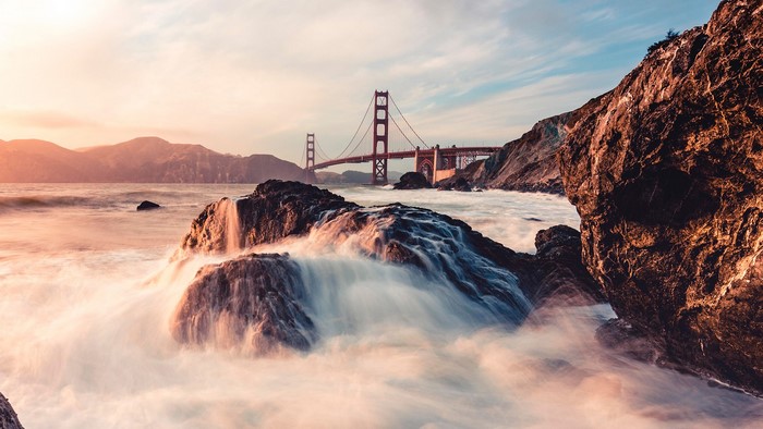 Golden Gate Bridge over ocean waves near rocks