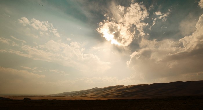 Sunlight breaking through clouds over sand dunes landscape