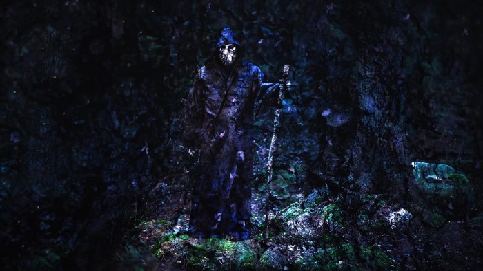 Figure in a dark forest with a staff