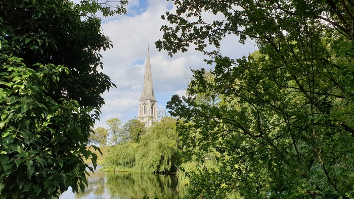 Church spire behind trees and pond