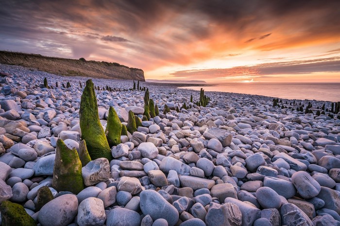 Pebble beach with wooden posts at sunset