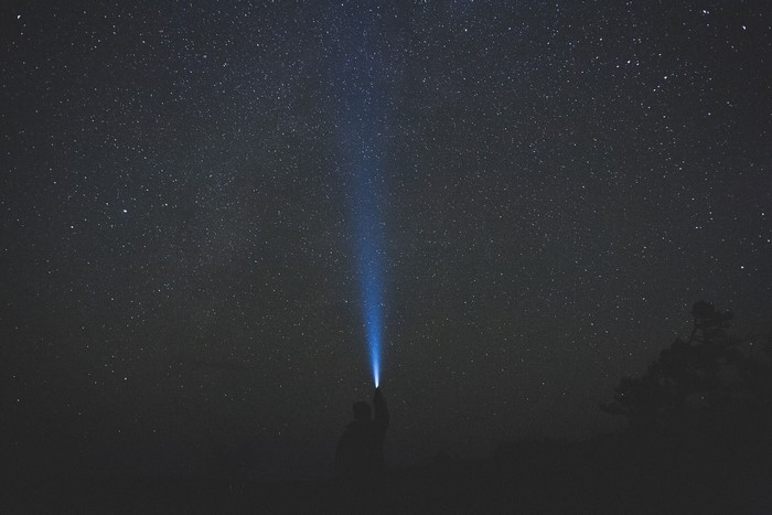 Person shining flashlight at starry night sky