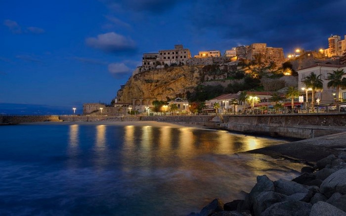 Town on a cliff overlooking the sea at night, Italy