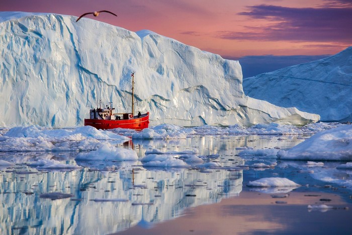 Red boat sailing near icebergs in Greenland