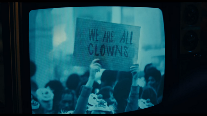 Joker holding a sign that says WE ARE ALL CLOWNS