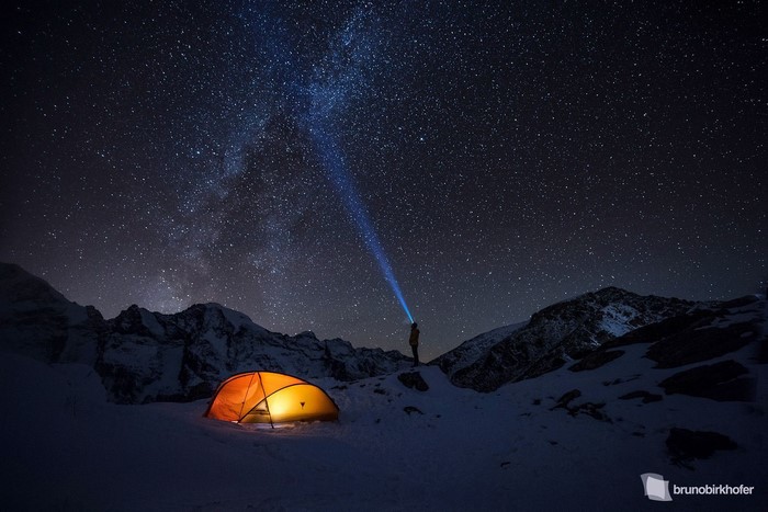 Man with flashlight under starry sky near tent