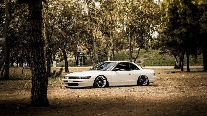 White JDM drift car parked in a park with trees