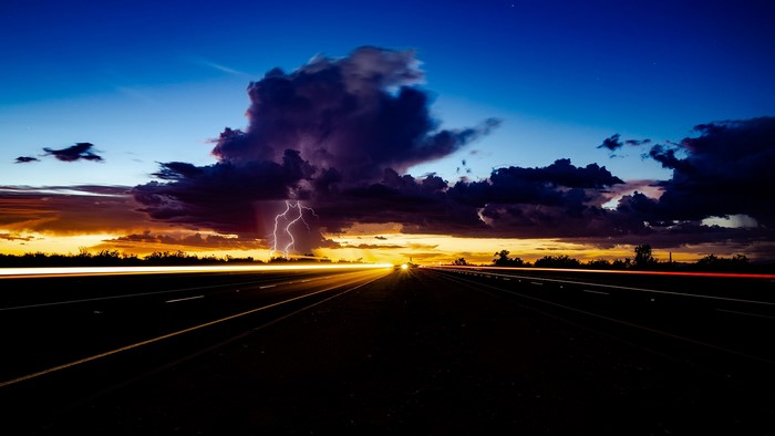 Lightning strikes over a highway at sunset