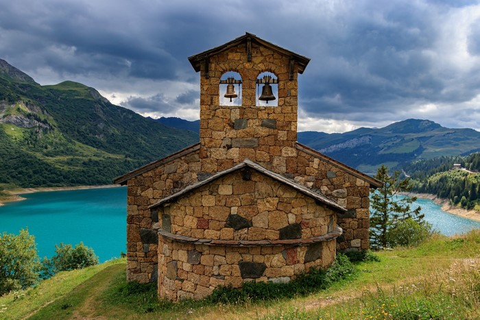 Stone church with bells by a turquoise lake in France
