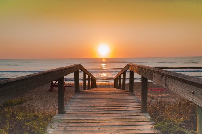 Wooden walkway to the beach at sunrise over the ocean