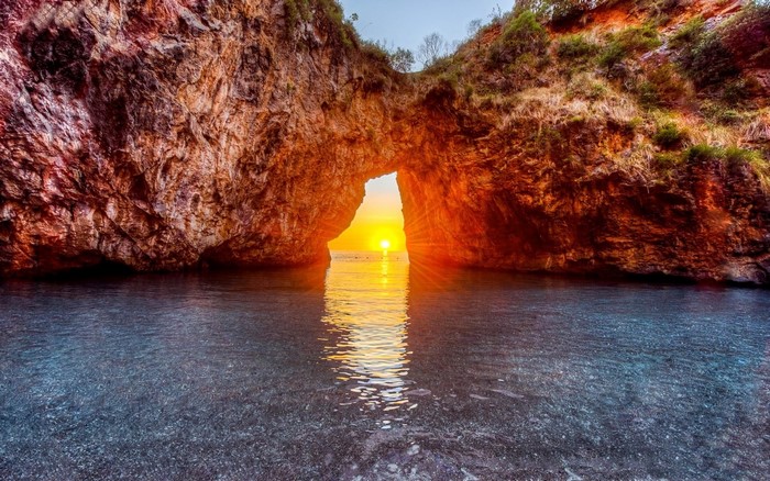 Sunset through Arcomagno rock arch in San Nicola Arcella, Italy