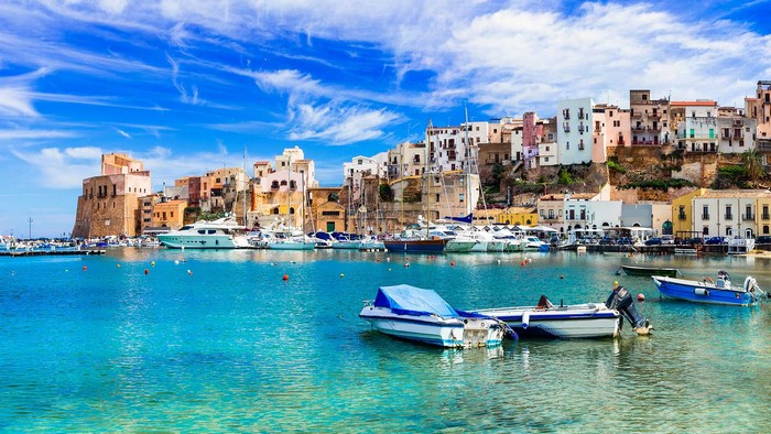 Boats in a harbor with colorful buildings in Sicily, Italy
