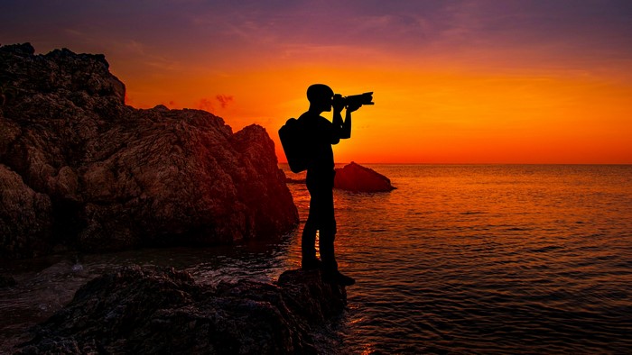 Photographer silhouetted against a sunset over the ocean