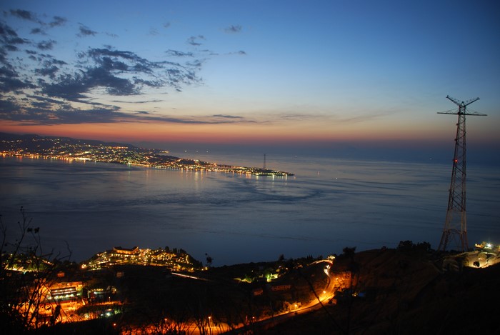 Strait of Messina at dusk with city lights and power tower