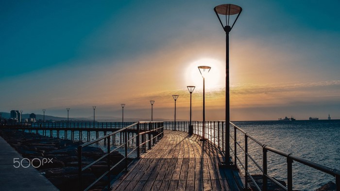 Pier with streetlights at sunset over the sea