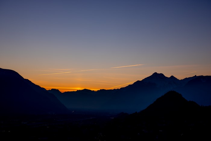Silhouette of mountains at sunset with contrails
