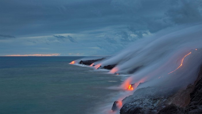 Lava flows into the ocean under cloudy skies