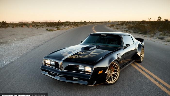 Black Pontiac Trans Am with gold decals on a desert road