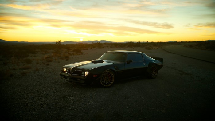 Black Pontiac Trans Am in desert at sunset