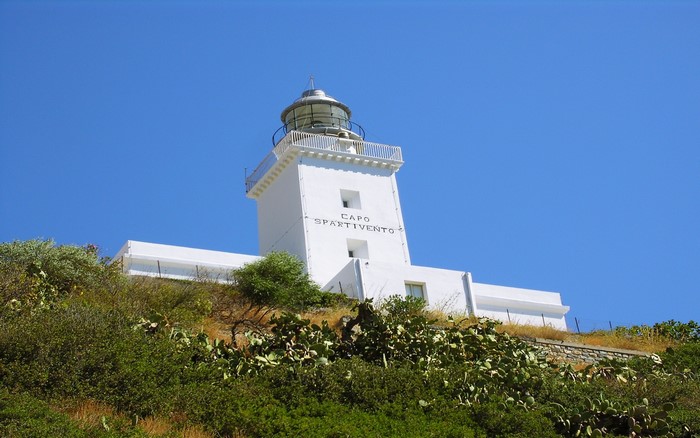 White lighthouse on a hill with vegetation under a blue sky
