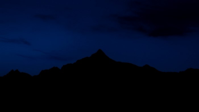 Silhouette of mountains against a dark blue night sky
