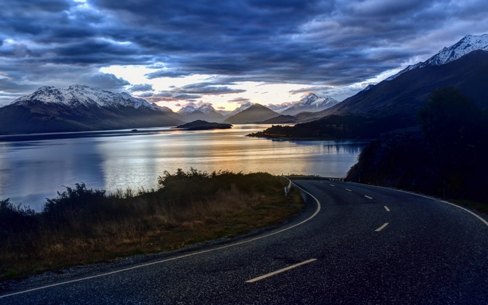 Winding road by a lake with snow-capped mountains