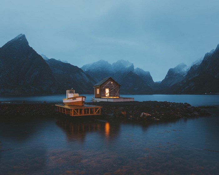 Cabin and boat by a lake with mountains at night